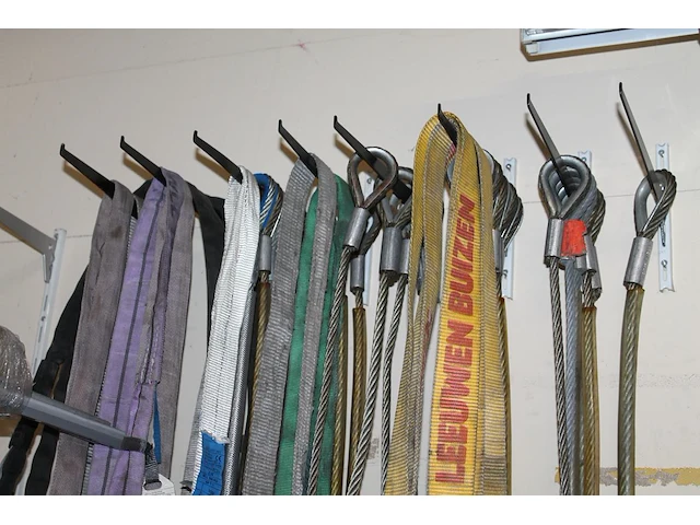 Grote hoeveelheid hijsbanden, staalkabels en ogen aan wand. - afbeelding 1 van  3