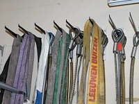 Grote hoeveelheid hijsbanden, staalkabels en ogen aan wand. - afbeelding 1 van  3