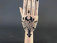 Gearticuleerde/gelede houten hand met een decoratieve, met de hand aangebrachte tatoeage-achtige illustratie van een chrysant op de handpalm en zwarte nagels - afbeelding 1 van  5