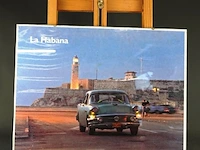 Ingelijste foto of poster getiteld "la habana" met een klassieke amerikaanse auto en de vuurtoren van het castillo de los tres reyes del morro in de achtergrond, gefotografeerd door guillermo bell in 2004