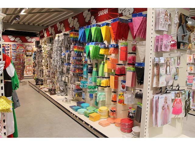 Kleurige feestartikelen aan 2 1/2 wandschap w.o. slingers, ballonnen, tafelkleden, borden en bestek. - afbeelding 1 van  5