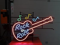 Neonreclame in de vorm van een elektrische gitaar met de tekst "rock & roll" en muzieknoten. werkend