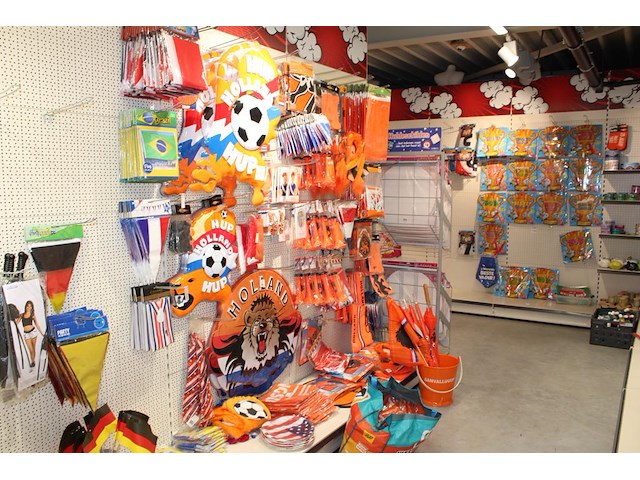 Oranje decoratie aan twee wandschappen w.o. vlaggen, borden, toeters, tassen, slingers en buttons. - afbeelding 1 van  5