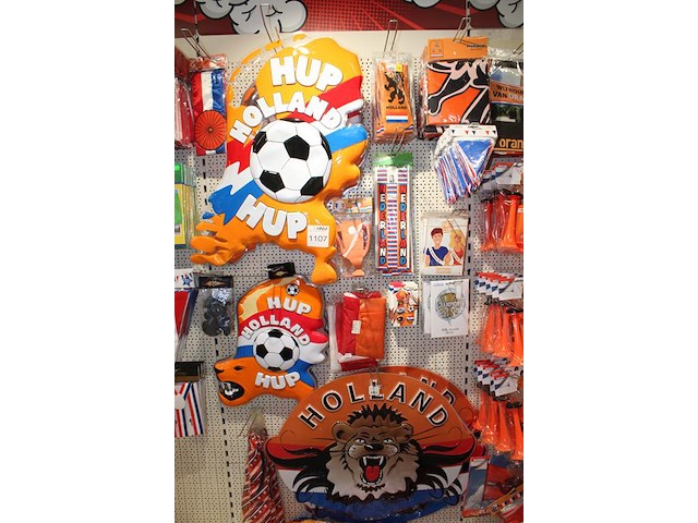 Oranje decoratie aan twee wandschappen w.o. vlaggen, borden, toeters, tassen, slingers en buttons. - afbeelding 4 van  5