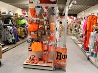Oranje producten op kopstelling en in winkelmand w.o. vlaggen, caps, mutsen, toeters, servies en brillen.