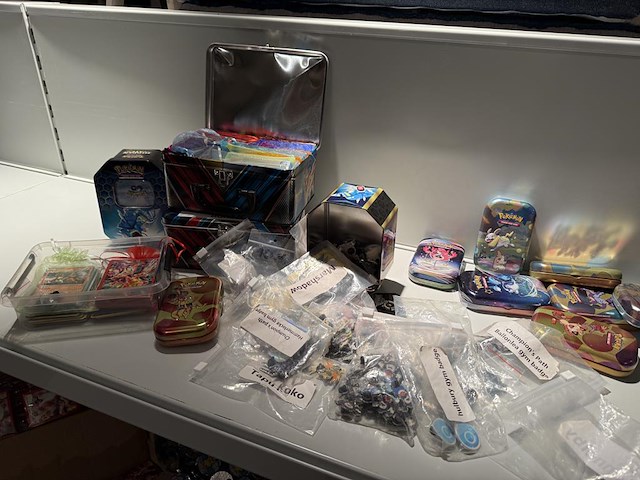 Pokemon producten op drie stellingschappen w.o. pokemon kaarten, pins pokemon blikken, pokemon verzamelmapp... onderdeel van combinatiekavel kavels p001 t/m p051 combinatiekavel - afbeelding 11 van  15