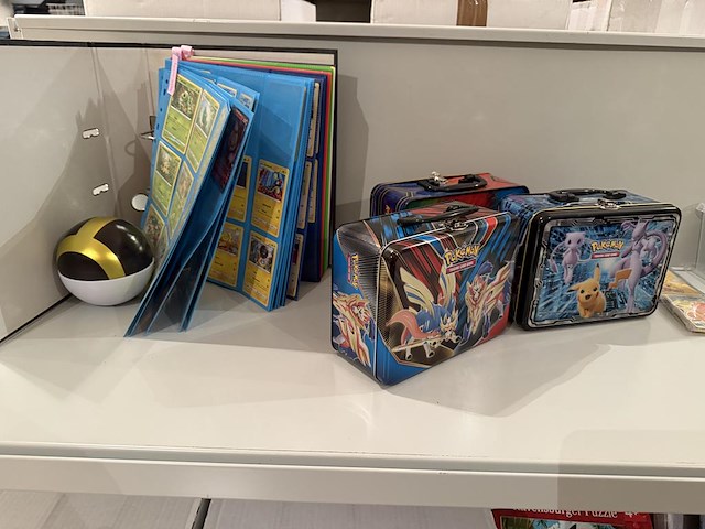 Pokemon producten op drie stellingschappen w.o. verzamelmappen, metalen koffertjes, puzzles, beschermzakjes... onderdeel van combinatiekavel kavels p001 t/m p051 combinatiekavel - afbeelding 14 van  18