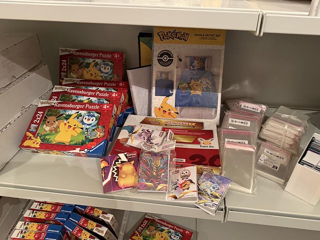 Pokemon producten op drie stellingschappen w.o. verzamelmappen, metalen koffertjes, puzzles, beschermzakjes... onderdeel van combinatiekavel kavels p001 t/m p051 combinatiekavel - afbeelding 16 van  18