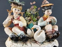 Porseleinen capodimonte beeldje van een jong stel omringd door zwanen, handbeschilderd in pastelkleuren